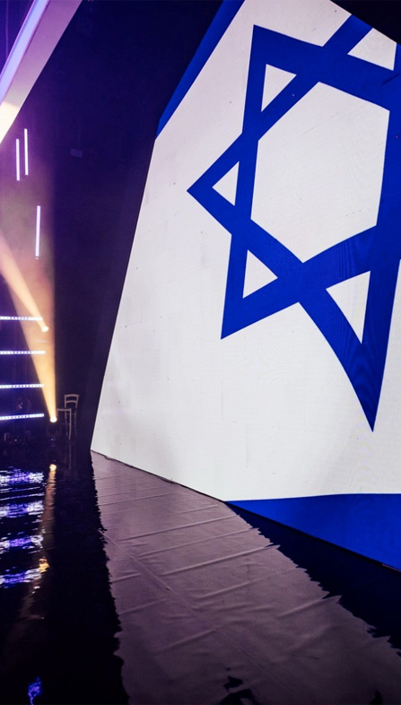 Israeli flag graphic on a large event stage screen.
